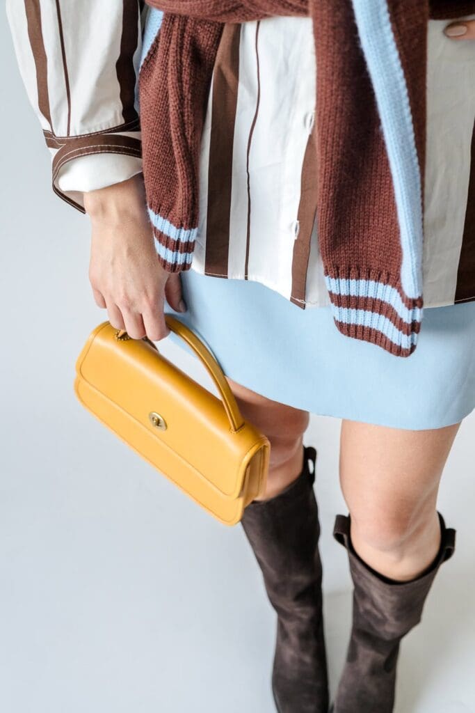 Detail shot of yellow clutch with statement boots and casual sweater tied at hips